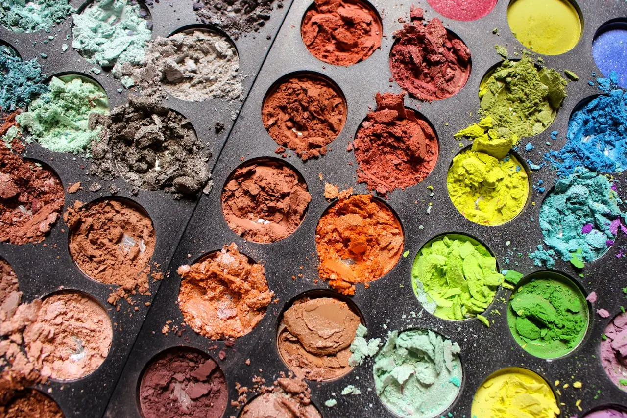 team-02 Close-up of a colorful eyeshadow palette with various shades and textures in a tray.