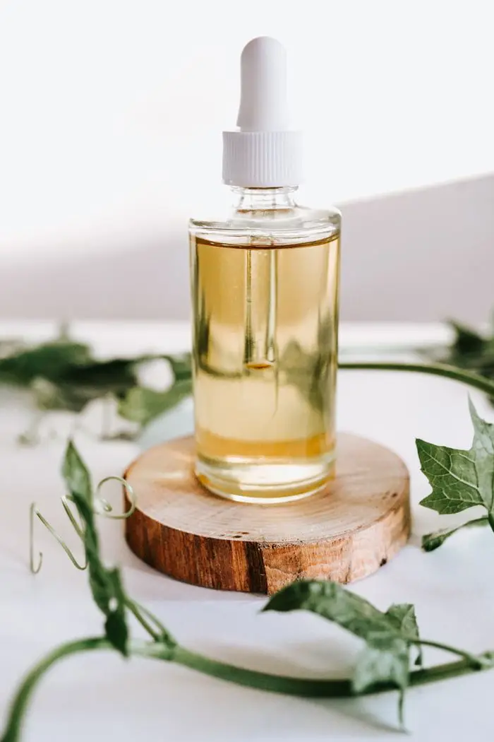 team-04 Close-up of essential oil dropper bottle on wooden stand surrounded by green leaves.